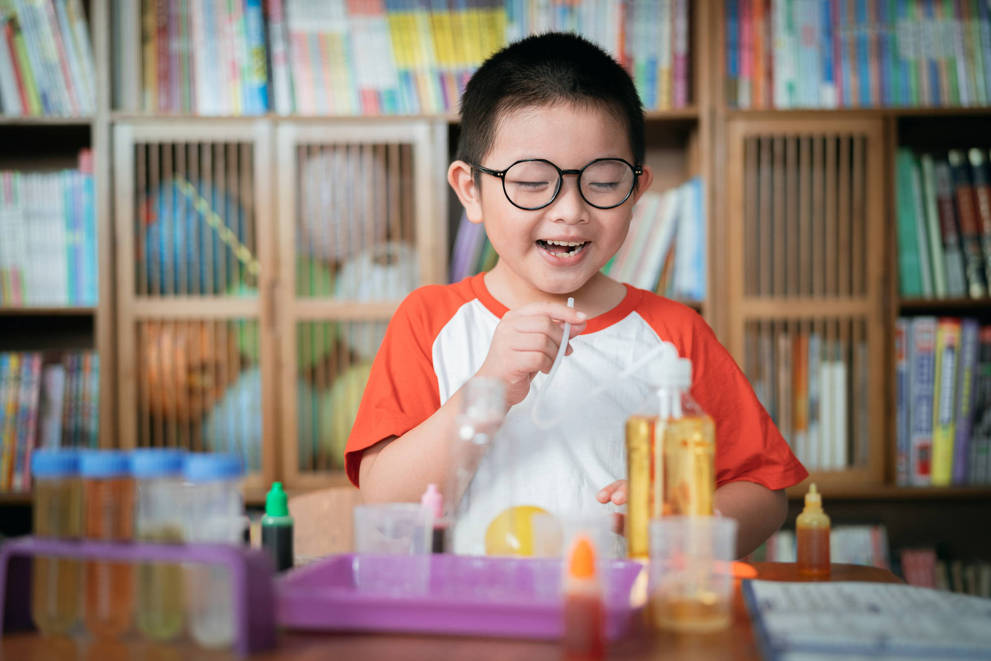 A young boy wearing glasses smiling happily while in a clasroom